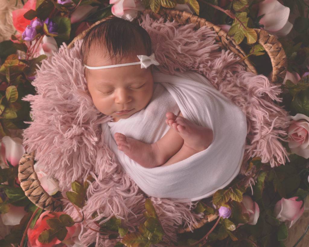 A newborn girl laying in a basket of flowers.