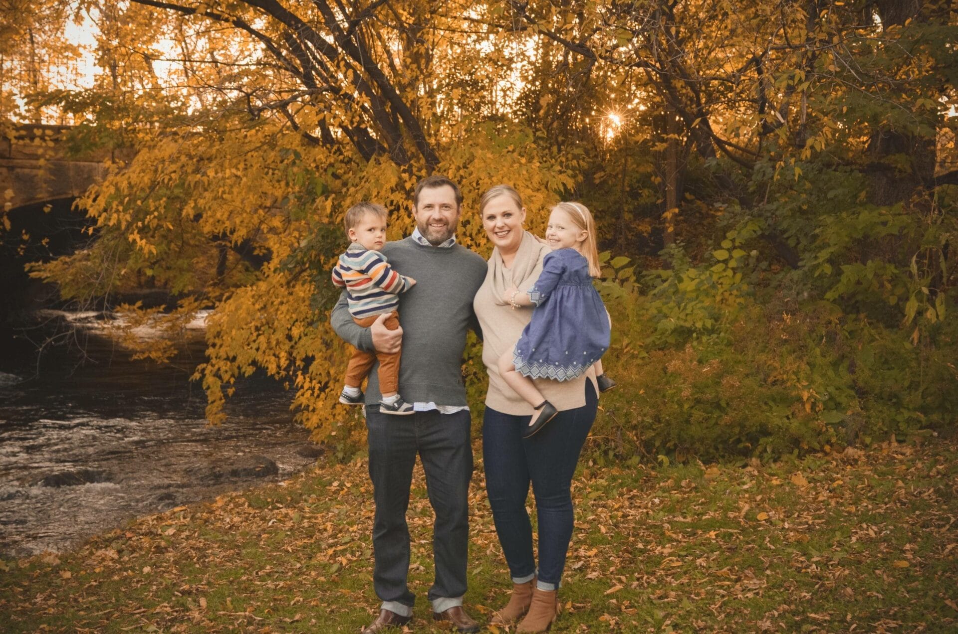A family posing in front of a river in the fall.
