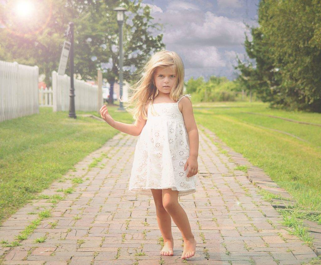 A little girl in a white dress standing on a brick walkway.