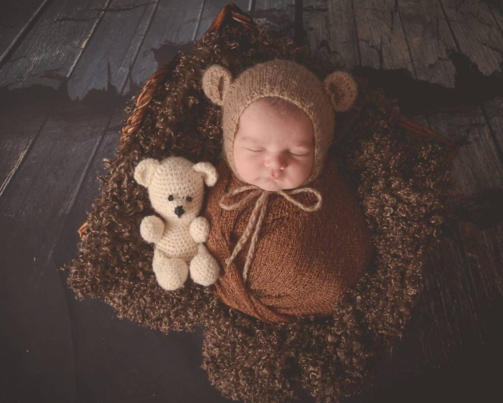 A newborn baby sleeping in a basket with a teddy bear.