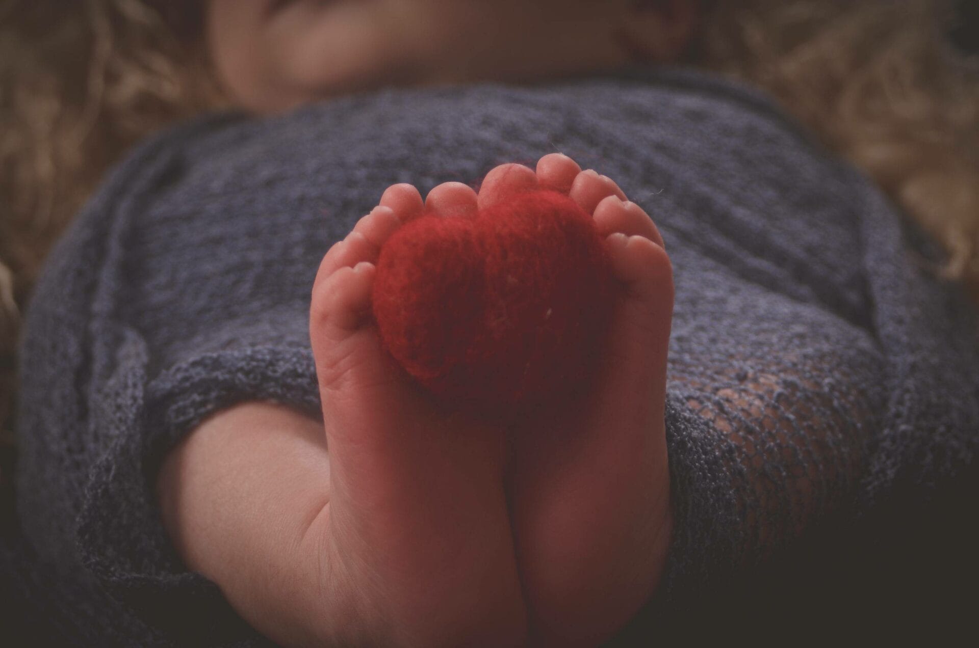 A baby's feet are wrapped in a blanket with a red heart.
