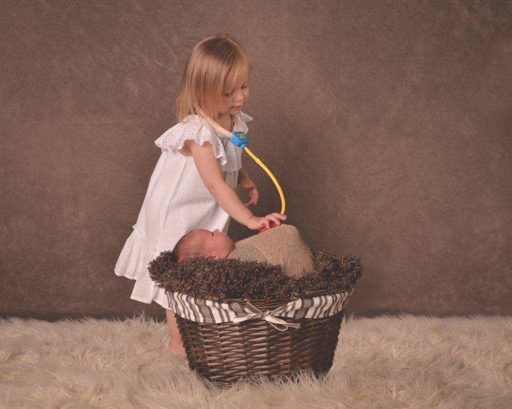 A little girl playing with a baby in a basket.