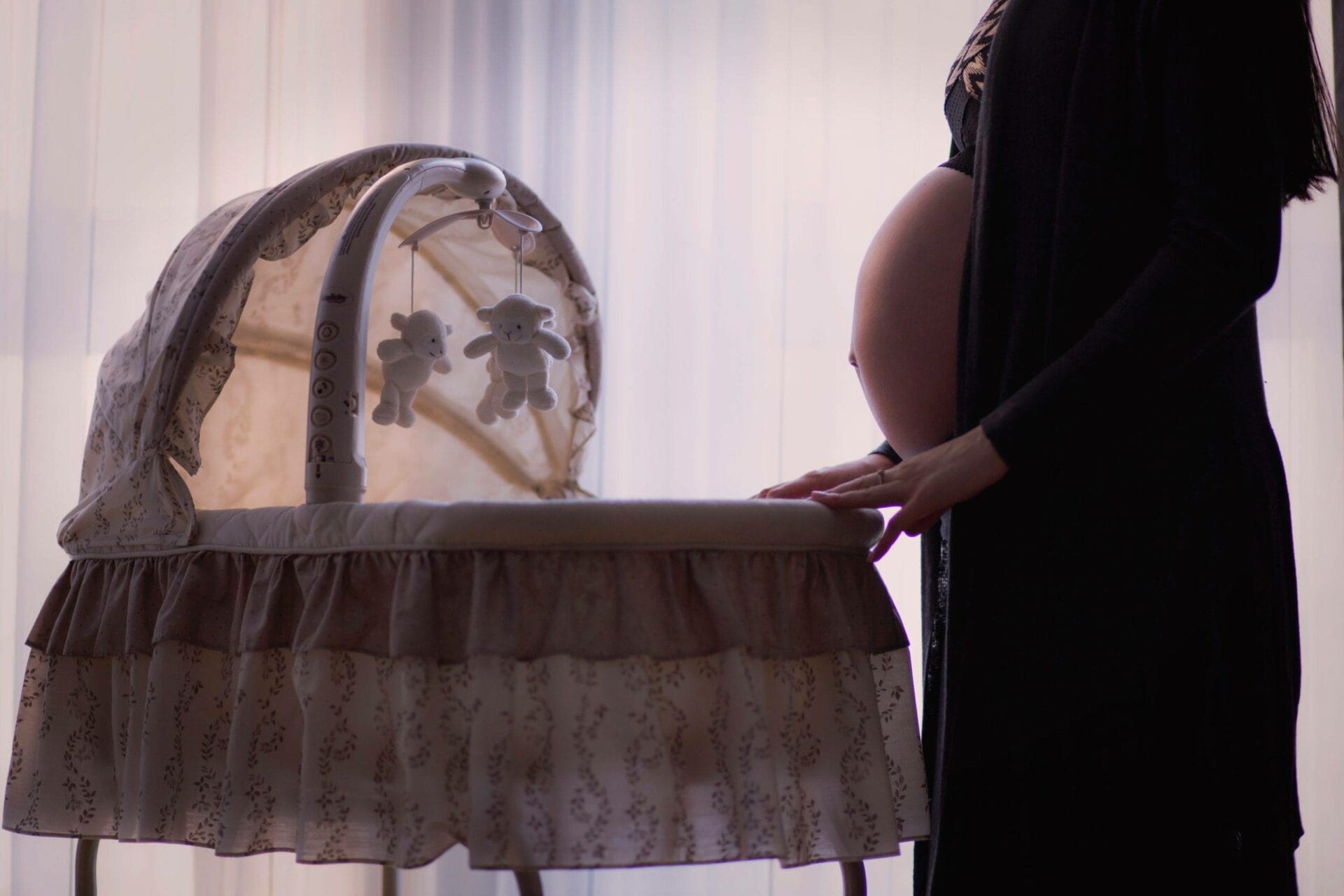 A pregnant woman standing next to a cradle.