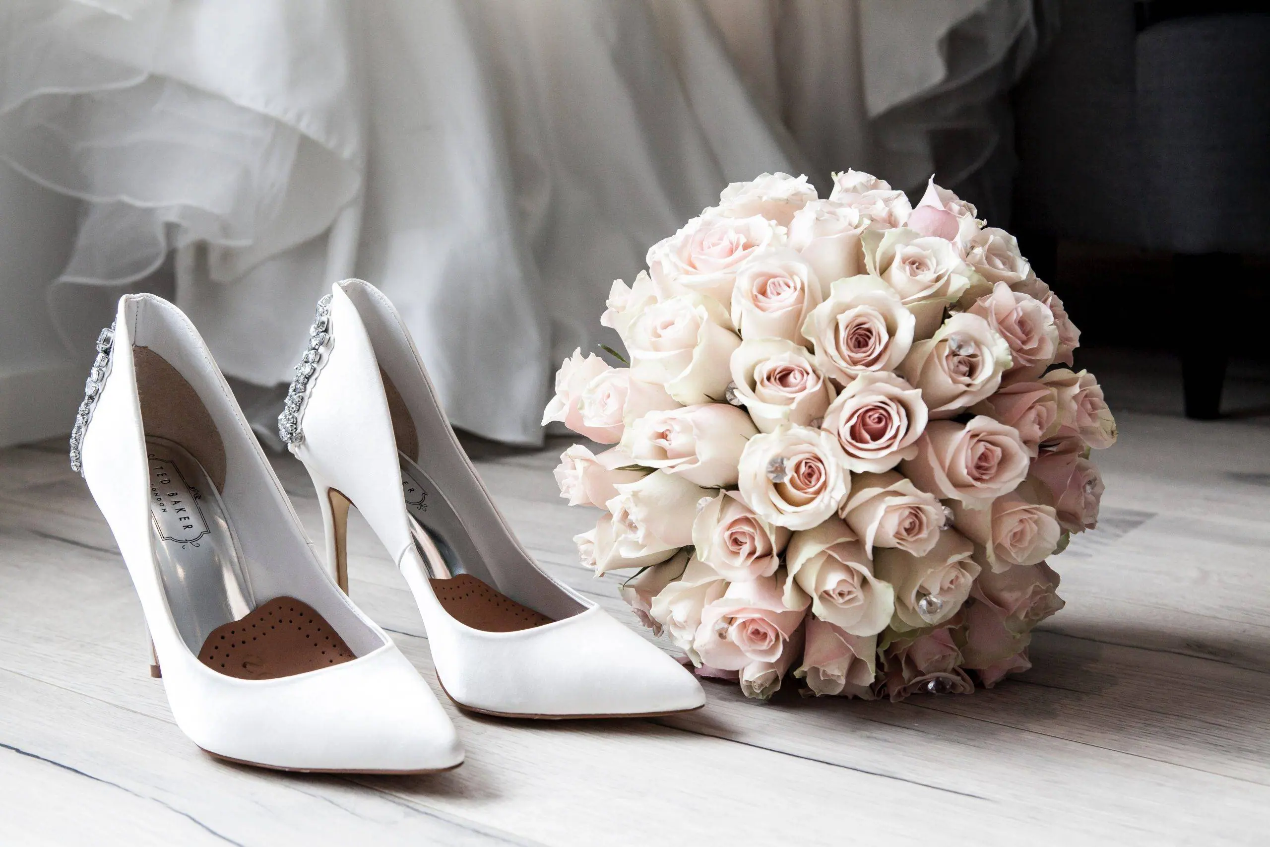 A bouquet of roses and wedding shoes on a wooden floor.