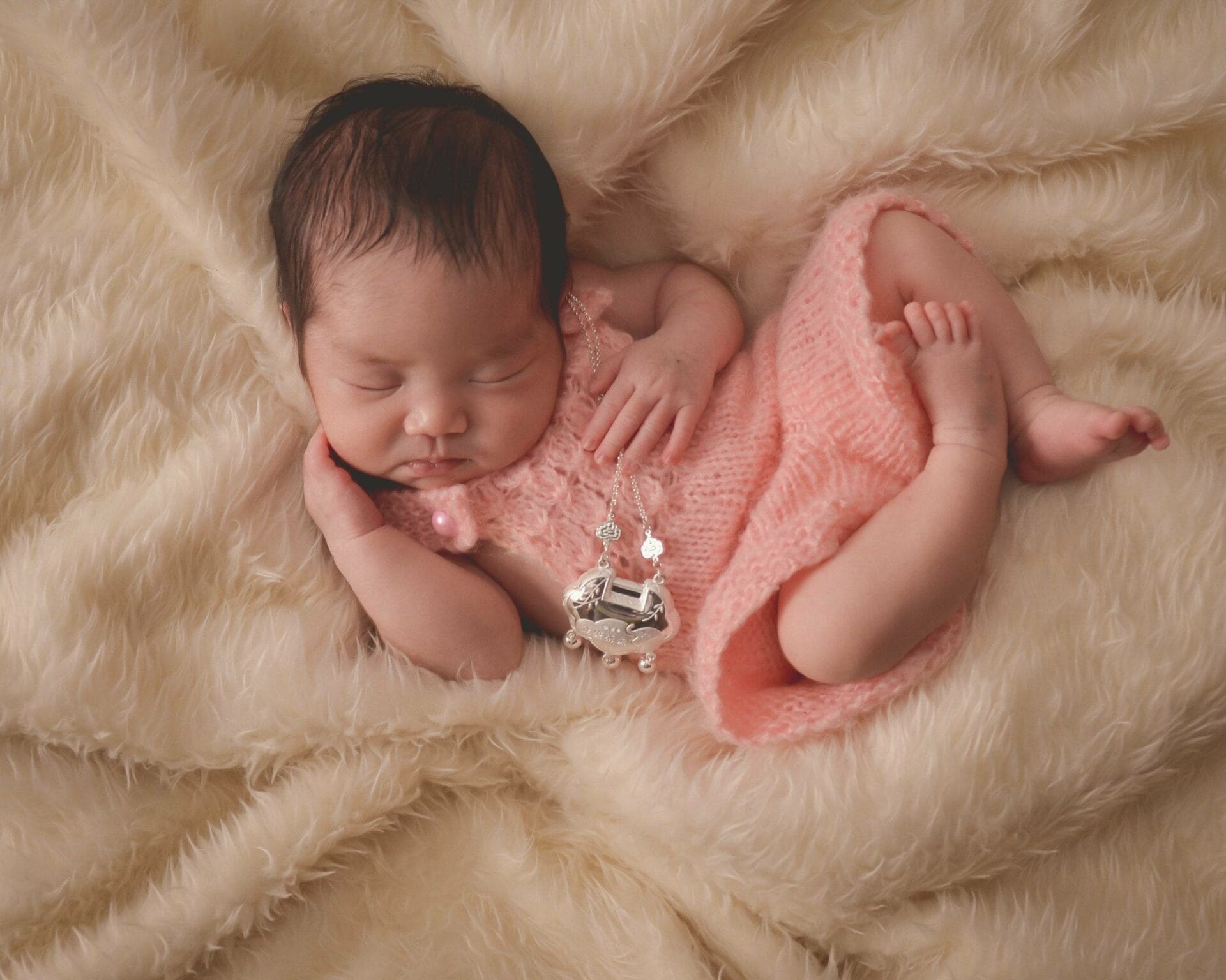 A baby girl in a pink dress laying on a fluffy blanket.