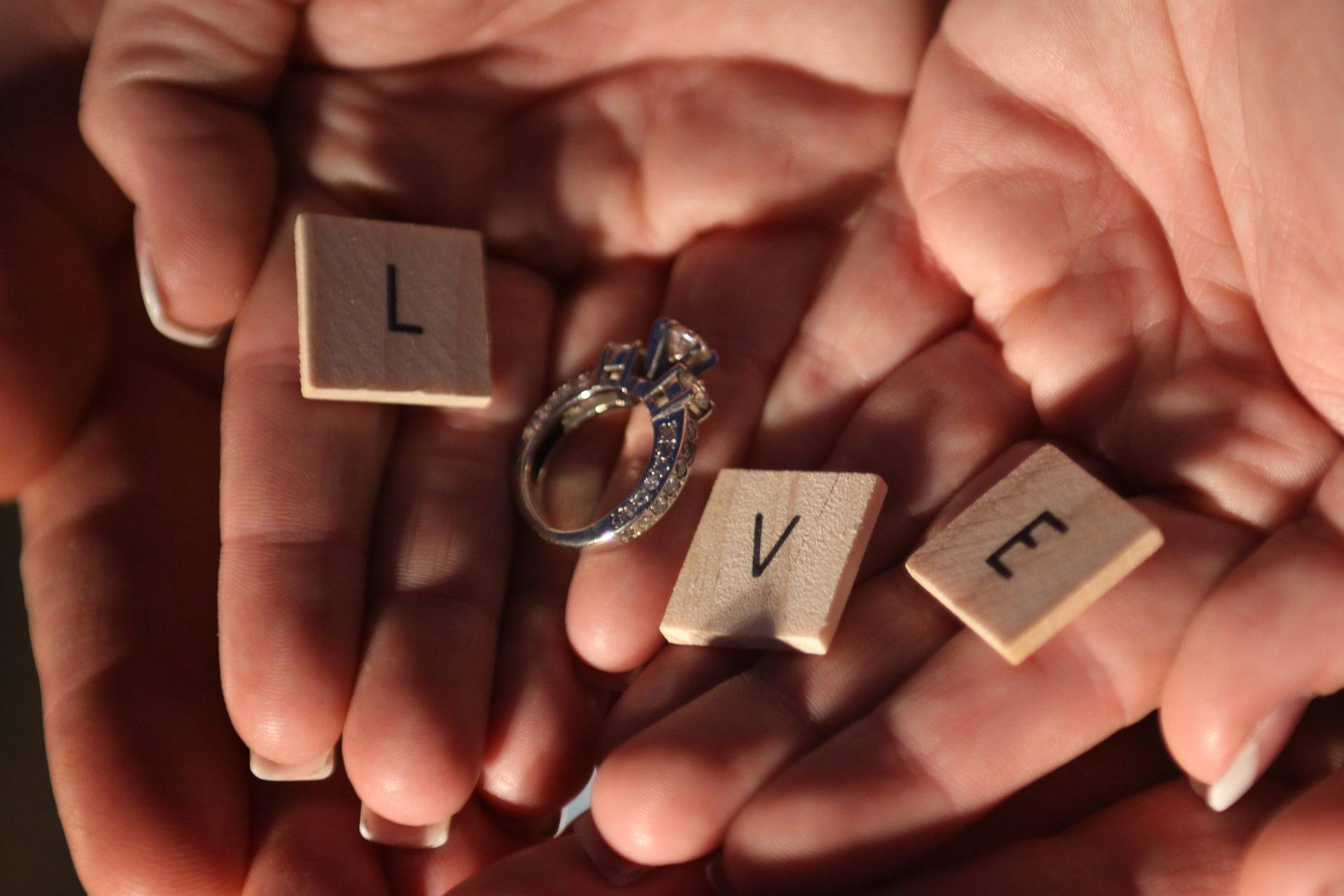 Two hands holding a wedding ring and scrabble letters.
