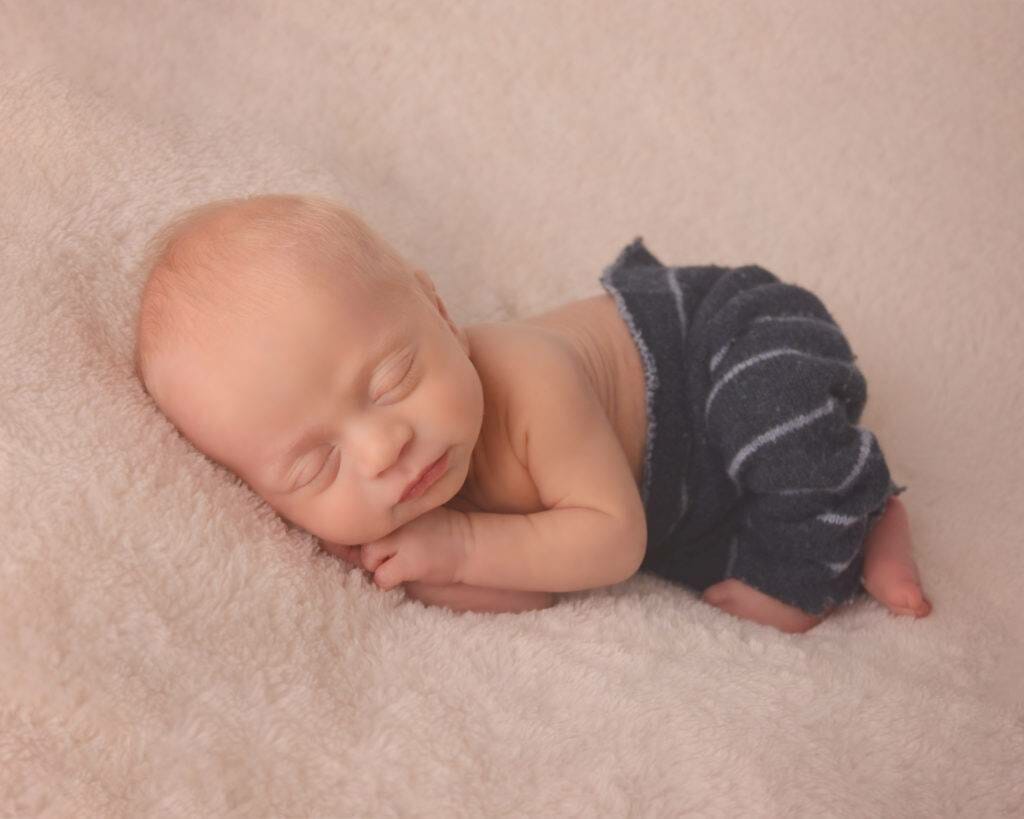 A newborn baby sleeping on a white blanket.