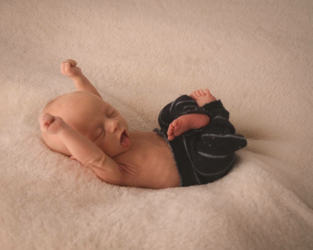 A baby is laying on a blanket with his arms up.