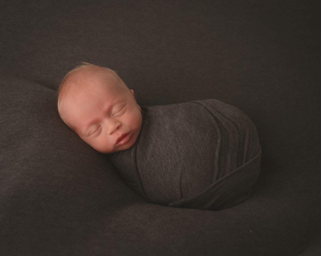 A newborn sleeping on a grey blanket.