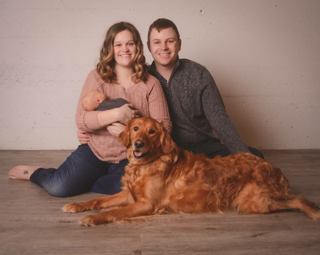 A man and woman are posing with their dog in front of a white background.