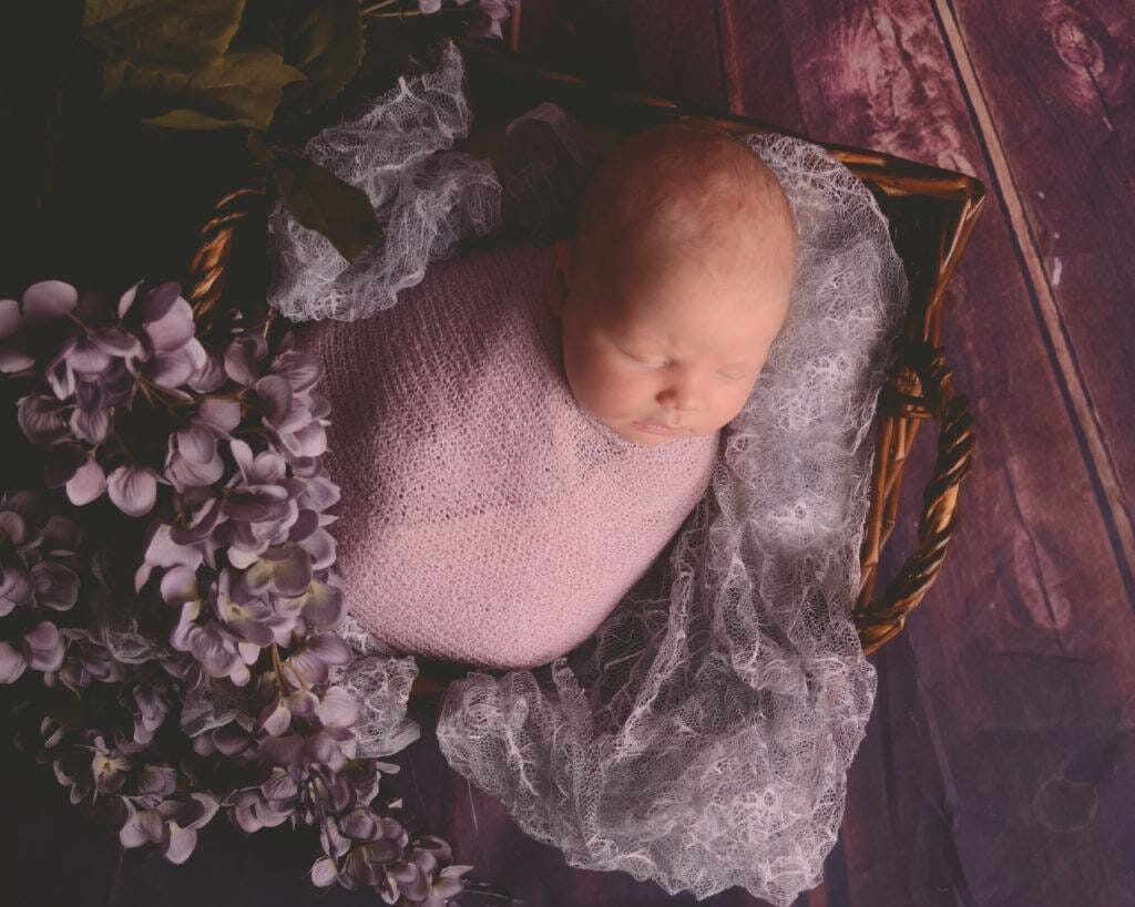 A newborn sleeping in a basket with purple flowers.