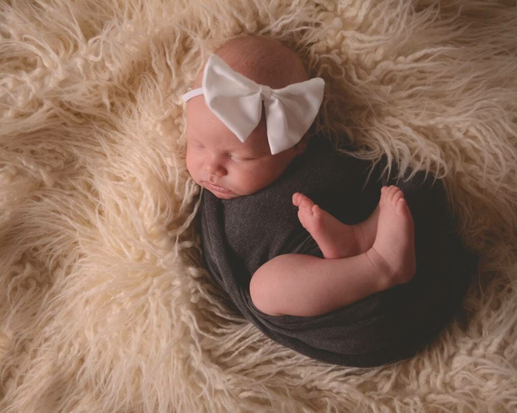A baby girl wrapped in a black blanket with a white bow.