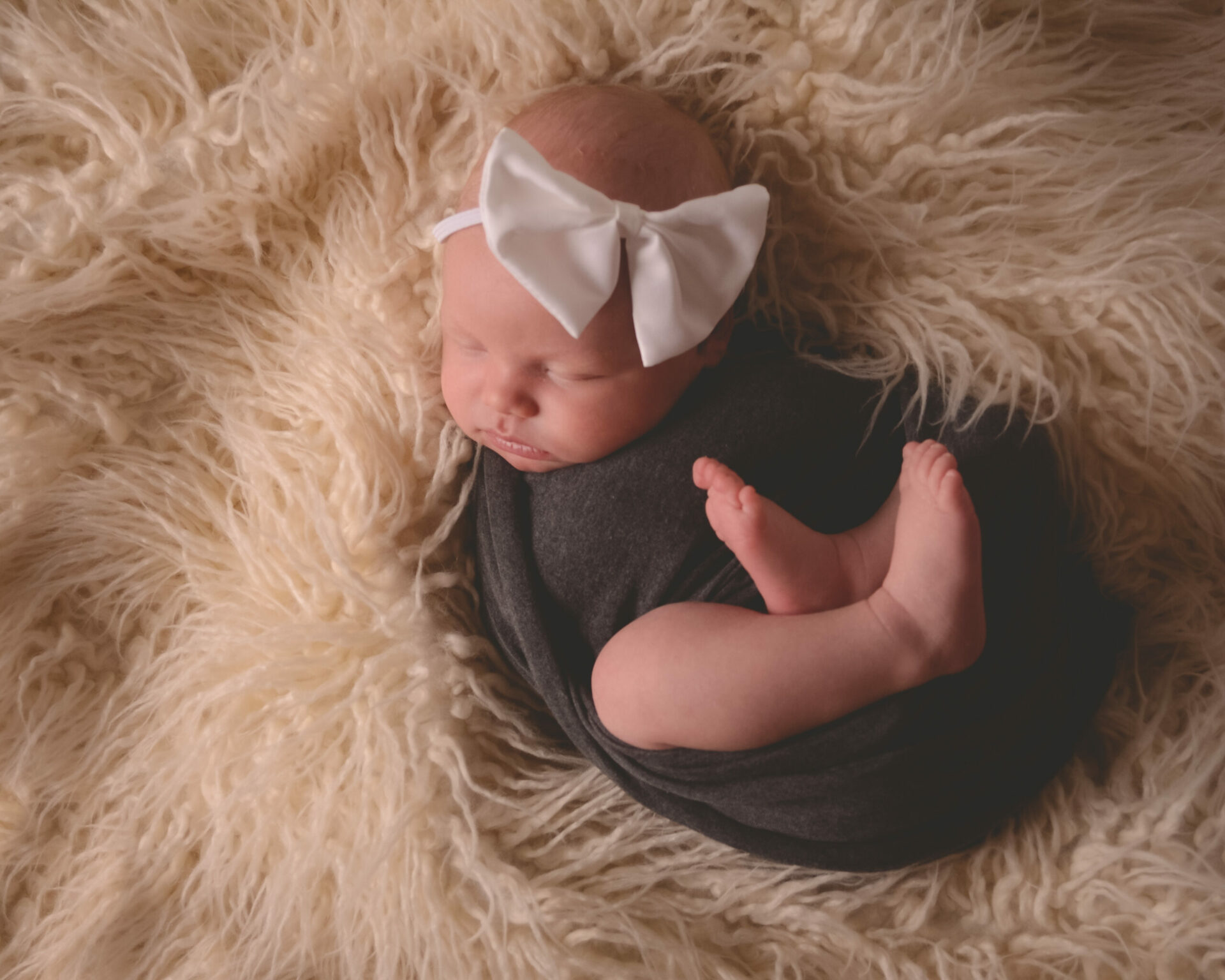 A baby girl wrapped in a black blanket with a white bow.