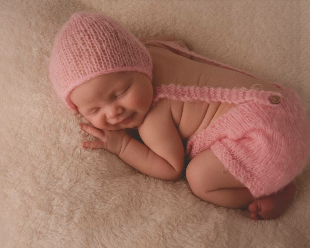 A baby sleeping in a pink knitted outfit.