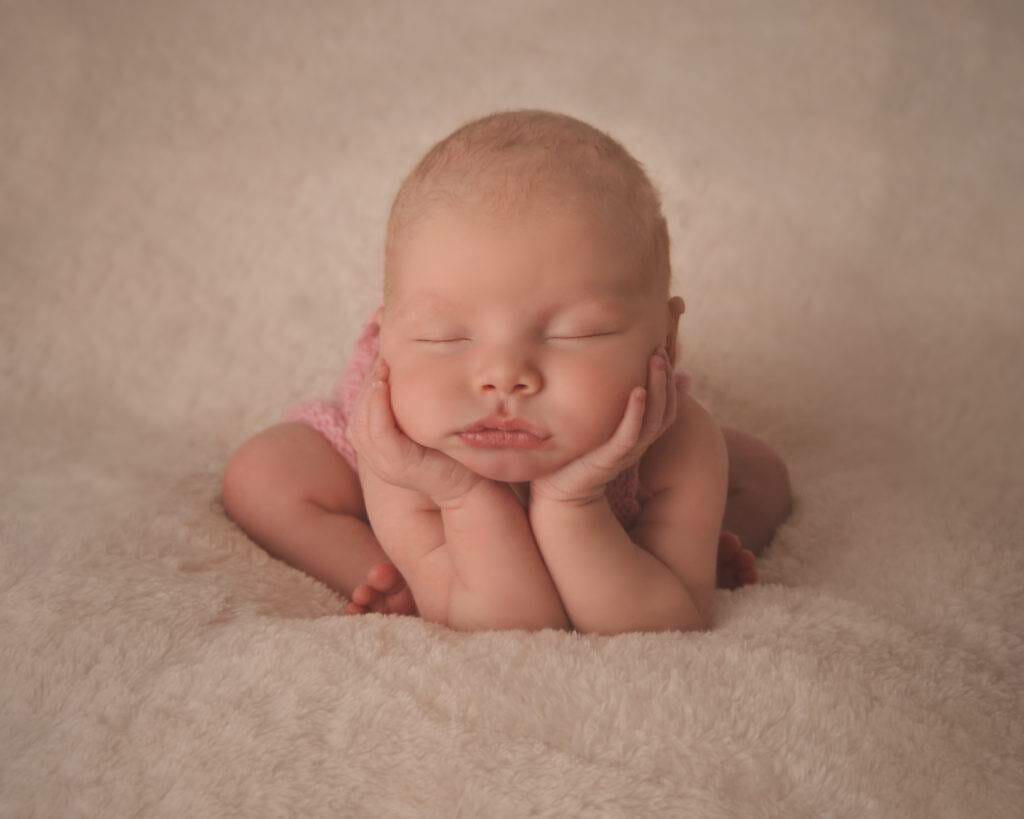 A baby girl is laying down on a white blanket.