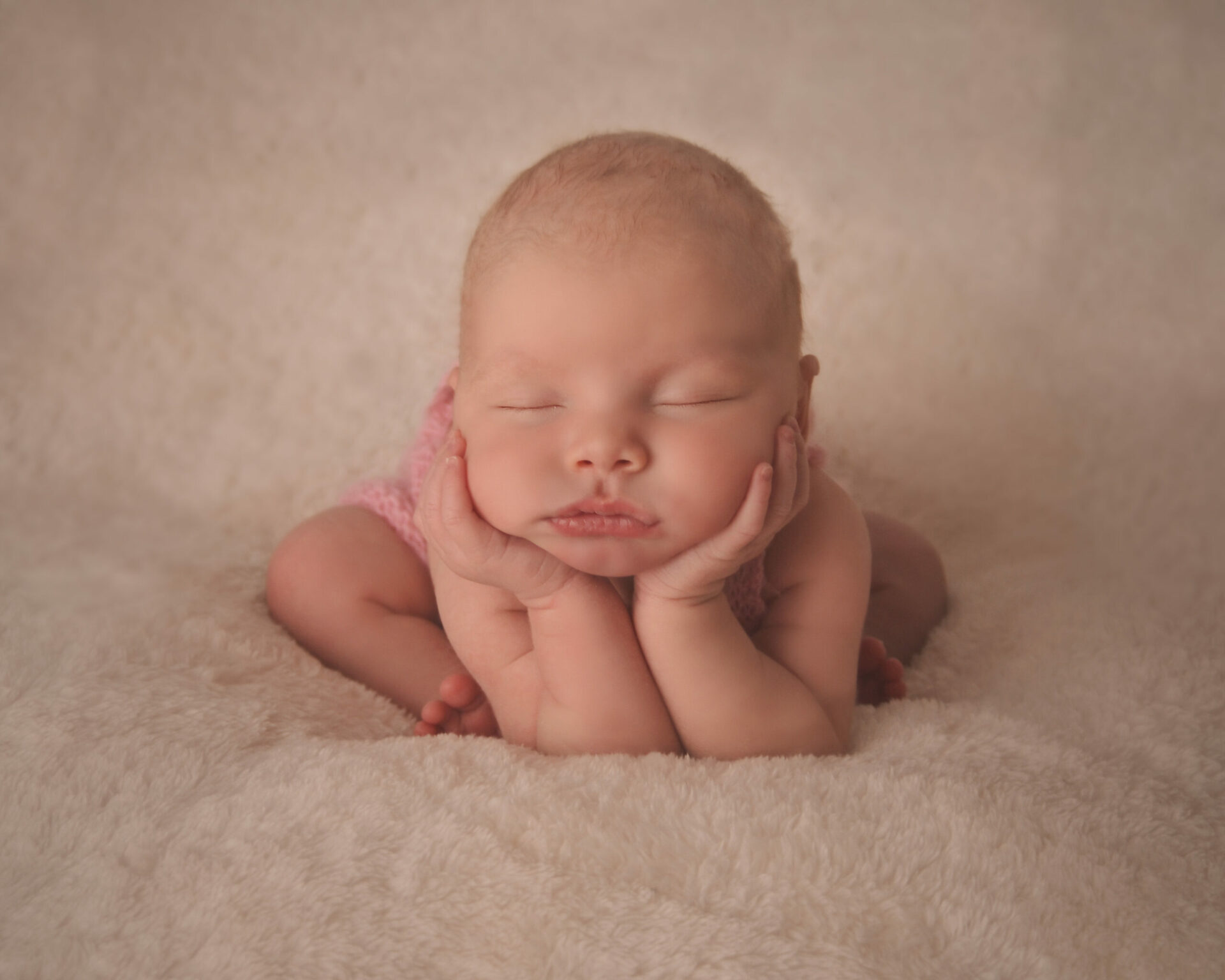 A baby girl is laying down on a white blanket.