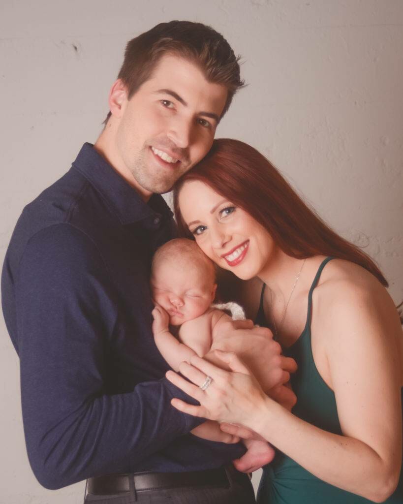 A man and woman posing with their newborn baby.