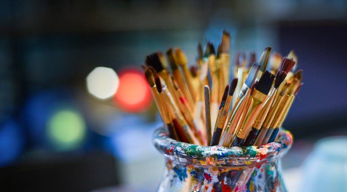 A vase full of paint brushes on a table.