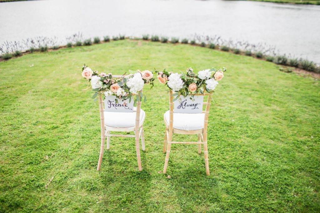 Two chairs are sitting on the grass next to a lake.