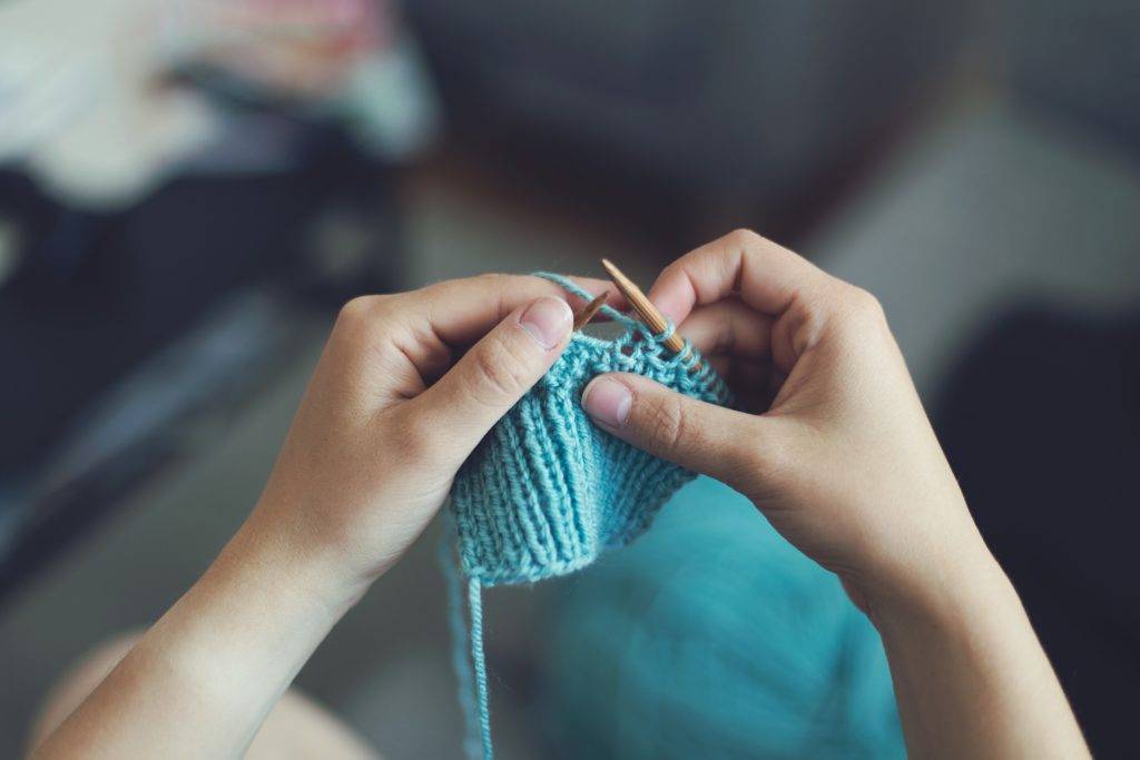 A person knitting a piece of blue yarn.