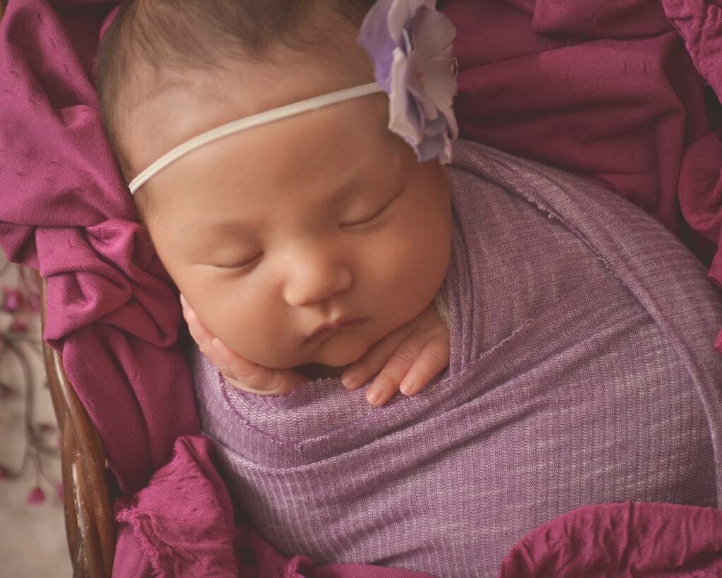 A newborn sleeping in a purple wrap.