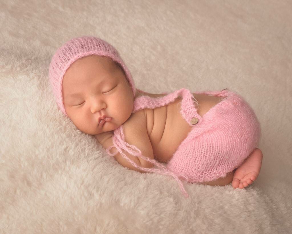 A newborn baby sleeping in a pink knitted outfit.