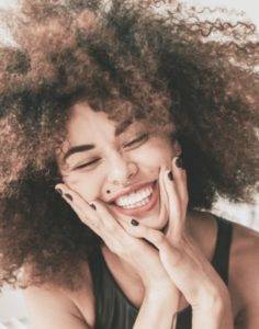 A woman with an afro smiles on a bed.