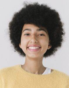 A young woman with an afro smiles in a yellow sweater.