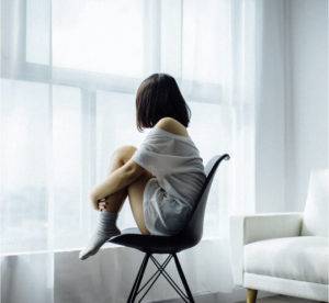 A woman sitting on a chair in front of a window.