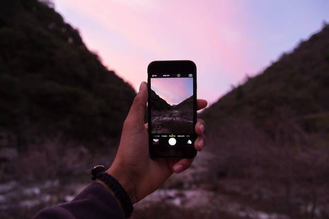 A person taking a photo with a smartphone in front of a mountain.