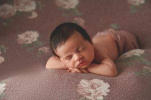 A newborn baby girl peacefully laying on a floral background in this stunning newborn photography session.
