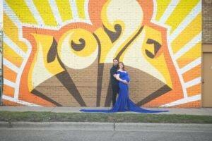 A couple posing in front of a mural with love written on it for their maternity photography session in Saint Paul, Minnesota.