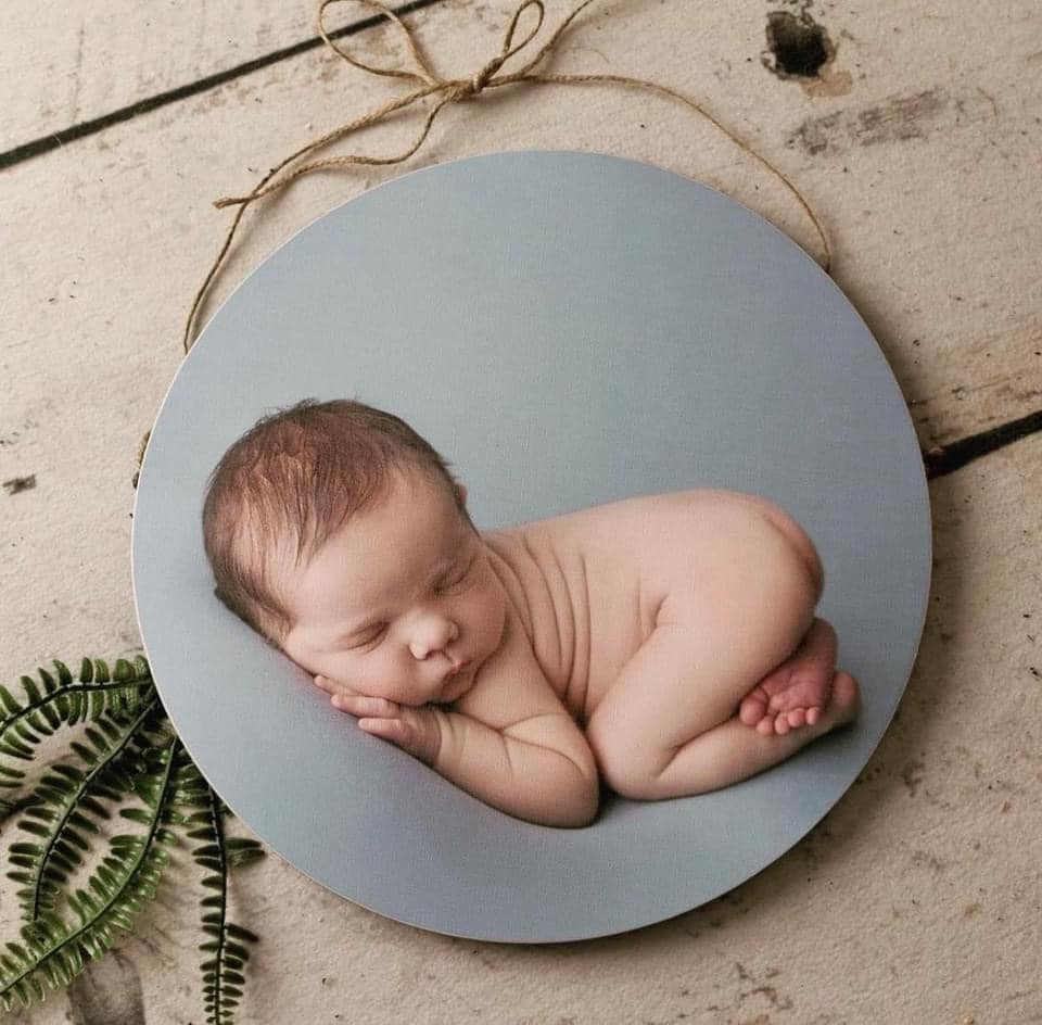 A photo of a baby laying on a wooden plaque.