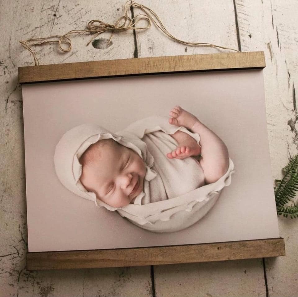 A photo of a baby wrapped in a blanket on a wooden frame.