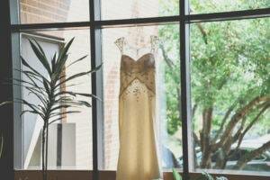 A wedding dress hanging in front of a window.