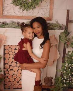 A mother and daughter posing in front of a christmas tree.