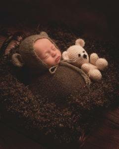 A baby sleeping in a basket with a teddy bear.