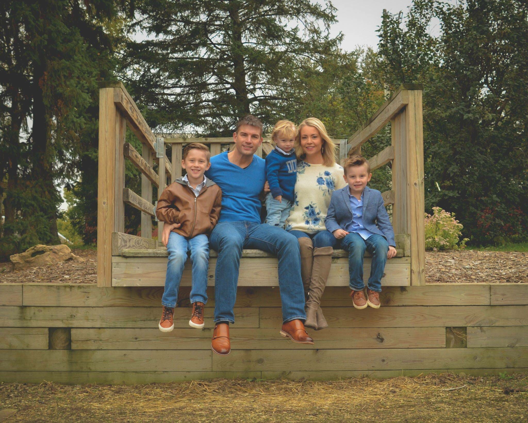 A family sits on a wooden bench in a wooded area.