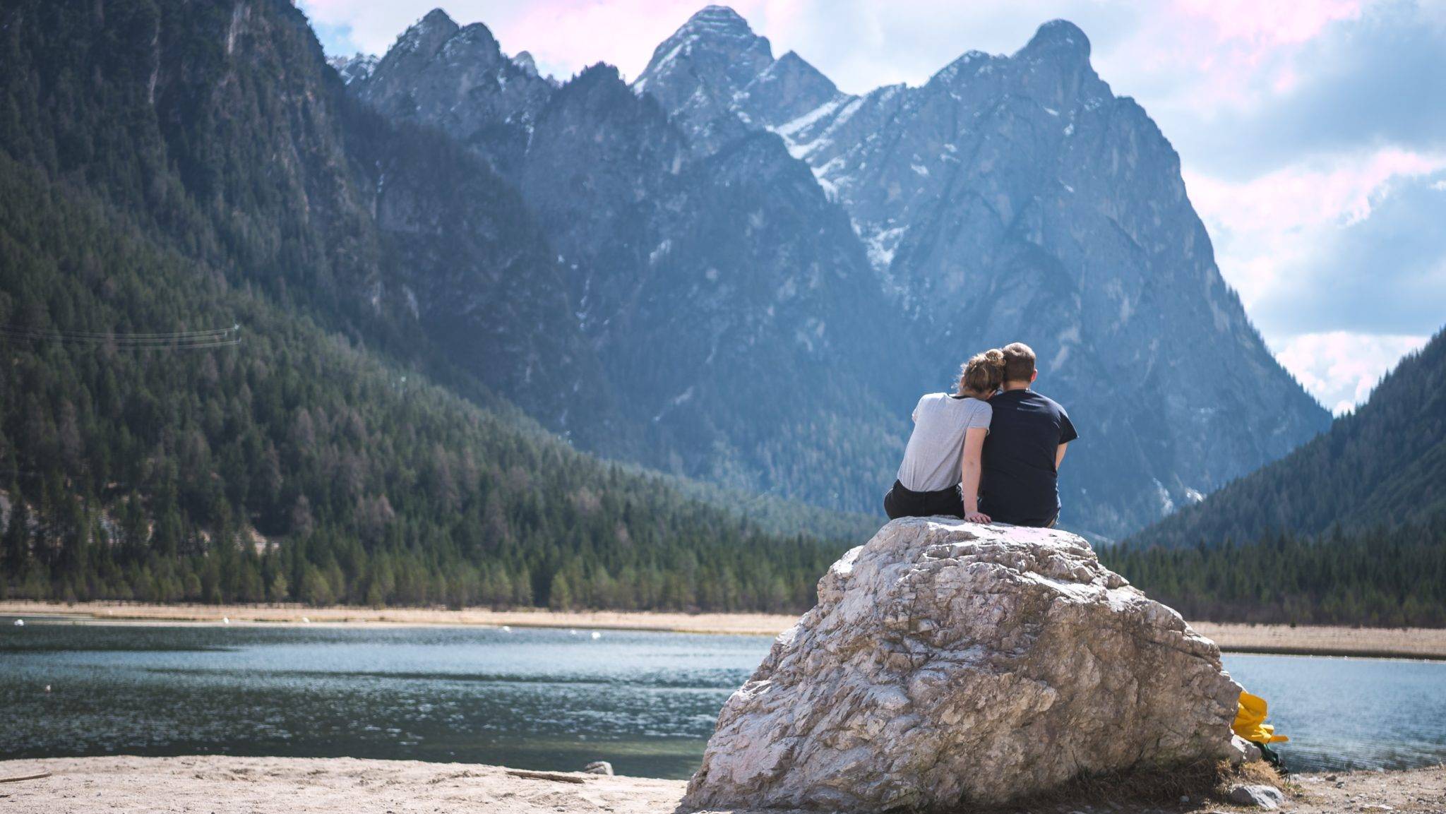 A couple sitting on a rock overlooking a lake.