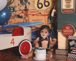 A baby is sitting in front of a cake with a toy car.