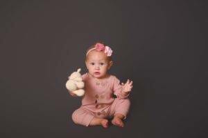 A baby girl holding a teddy bear on a gray background.