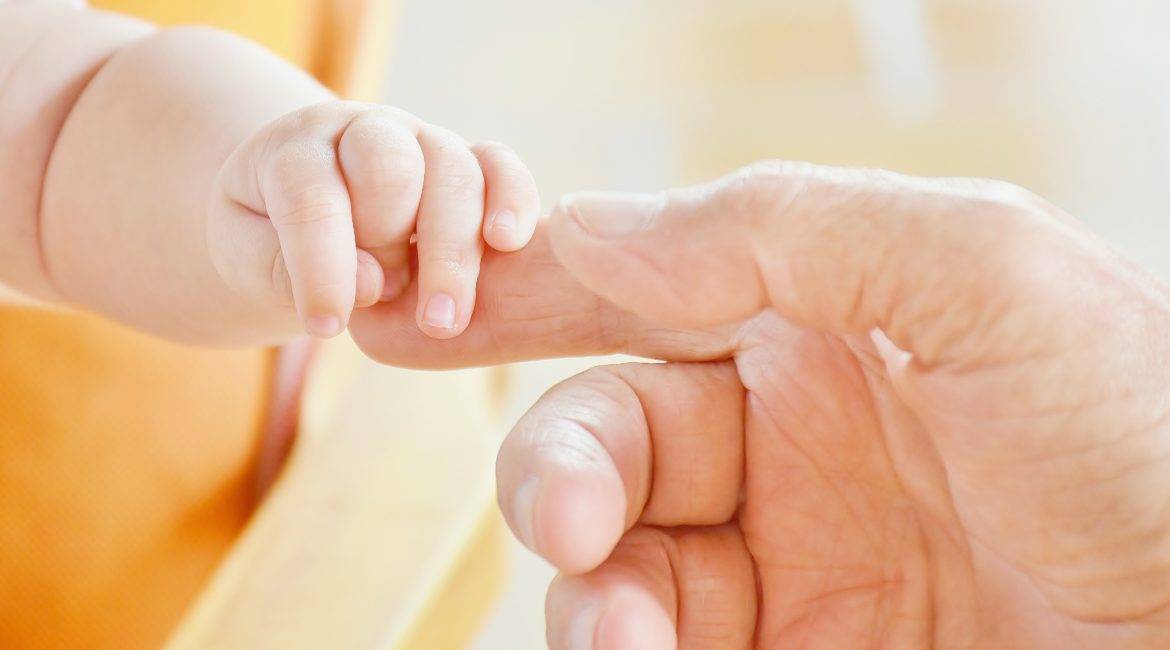 A baby's hand is being held by an older man.