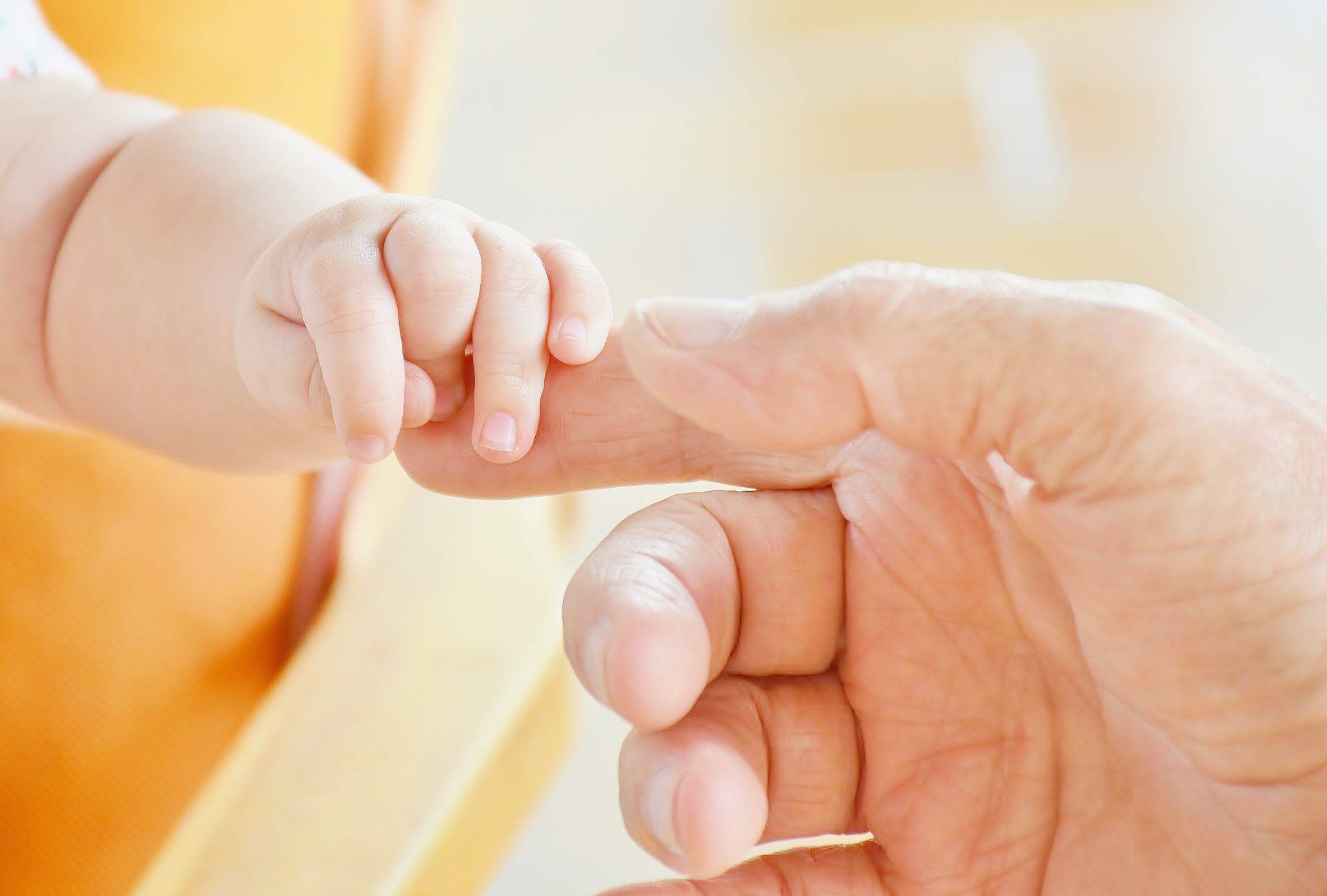 A baby's hand is being held by an older man.
