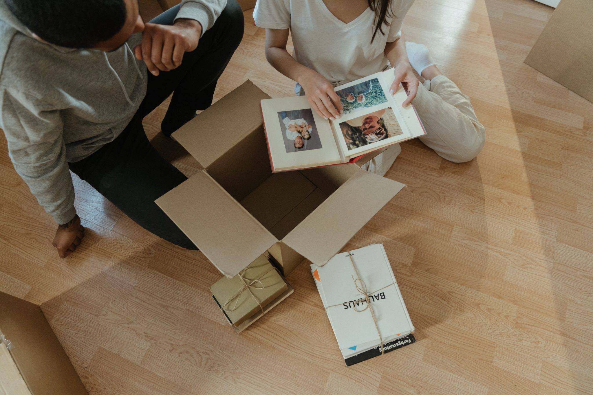 A man and woman sitting on the floor in front of a cardboard box.