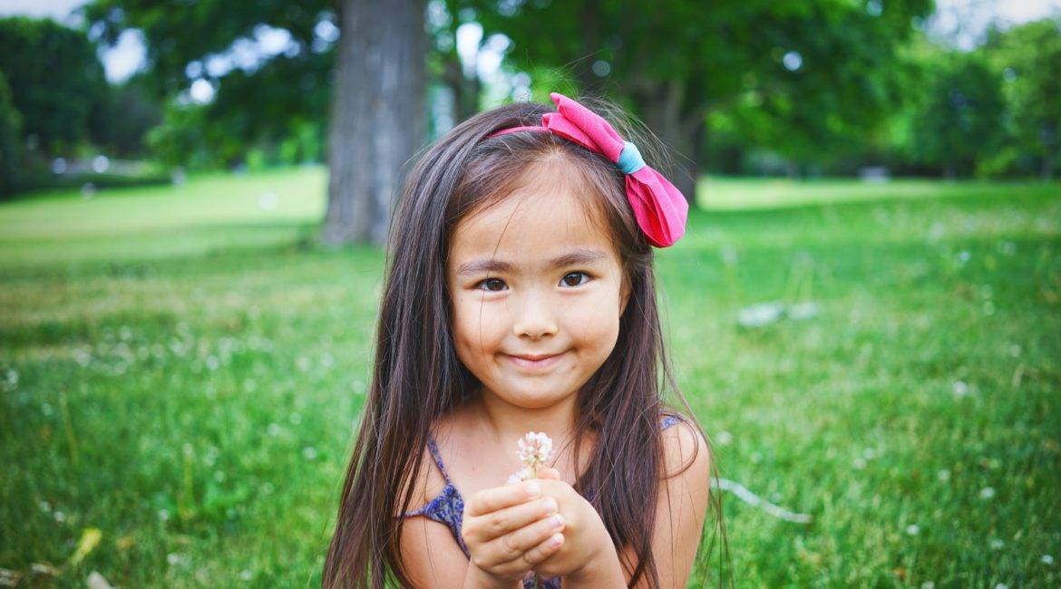 A little girl is sitting on the grass and holding a flower.