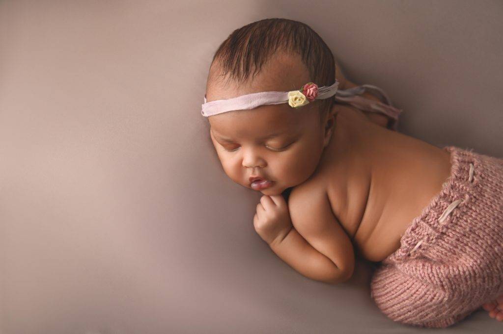 A newborn baby sleeping in a pink outfit.