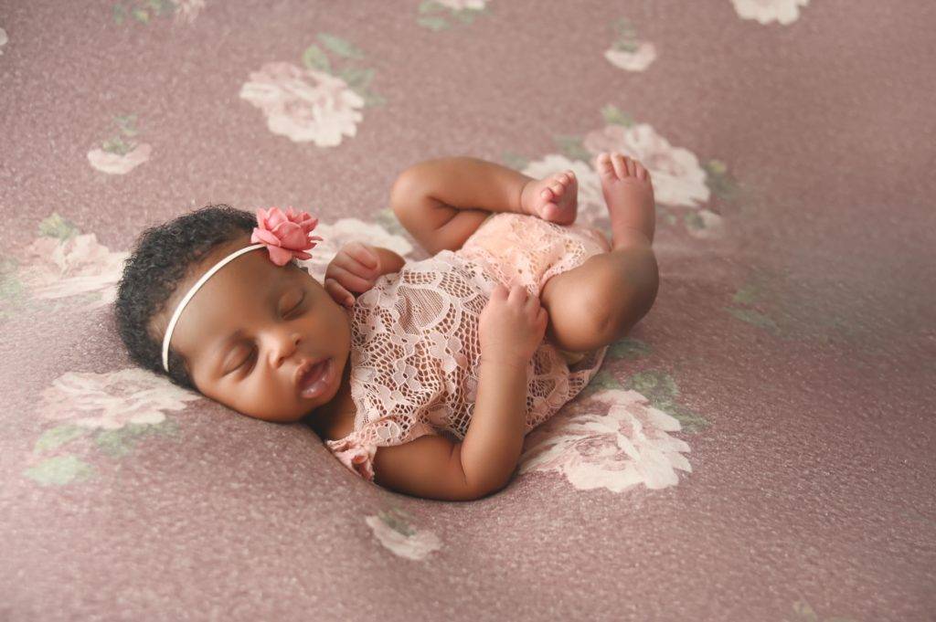 A baby girl is laying on a pink floral background.