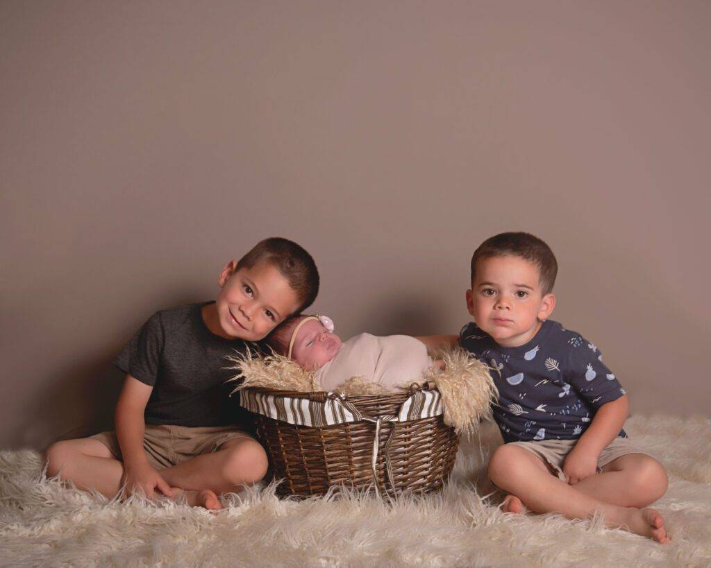 Three boys sitting in a basket with a newborn in it.