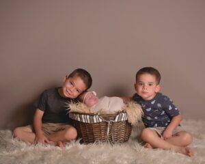 Three boys sitting in a basket with a newborn baby in it.