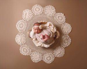 A baby girl is laying in a basket with a doily.